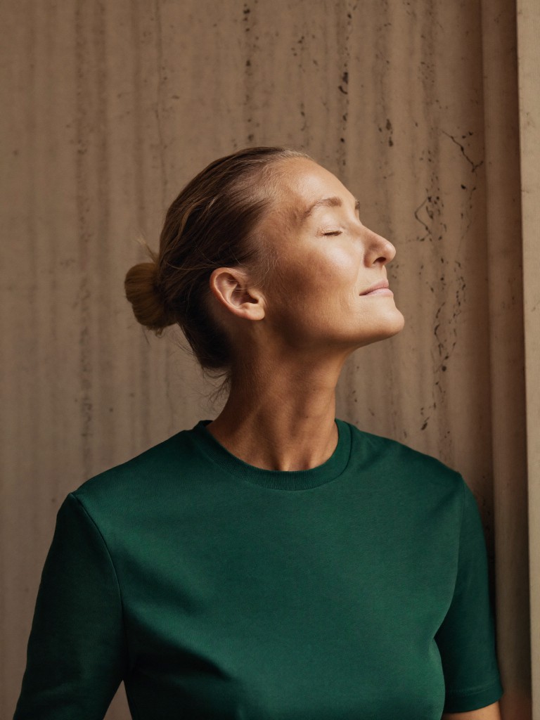 Woman in a forest green shirt with eyes closed against a textured stone wall