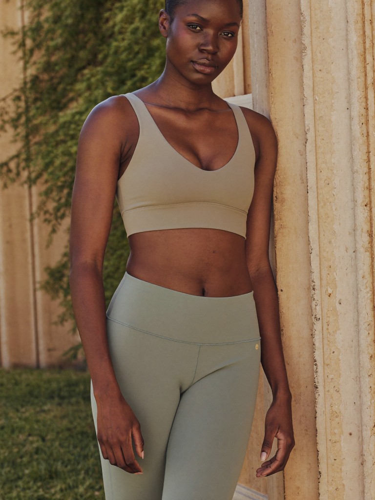 Woman in tan and sage athletic wear leaning against a stone column outdoors