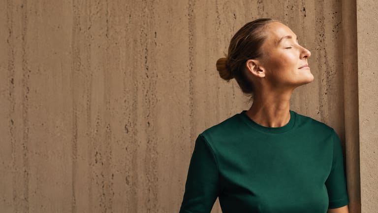 A woman resting against a travertine wall in daylight