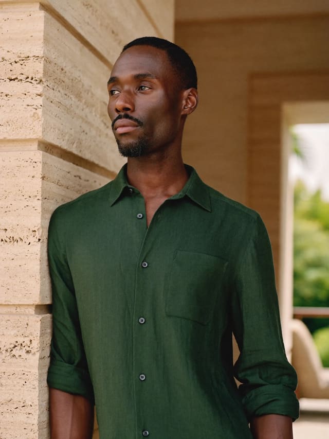Model in a forest-green shirt leaning against a travertine wall