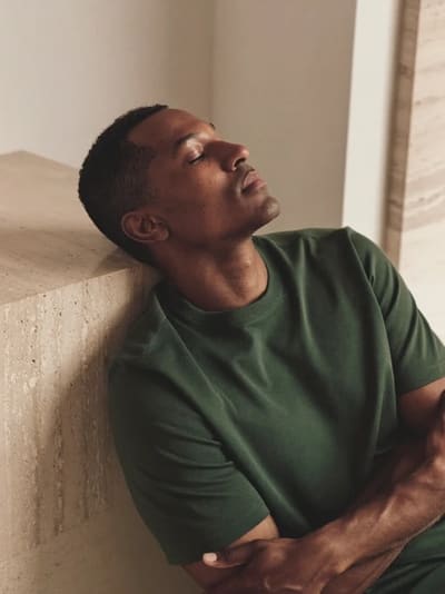Model in a green T-shirt resting against a stone block, eyes closed