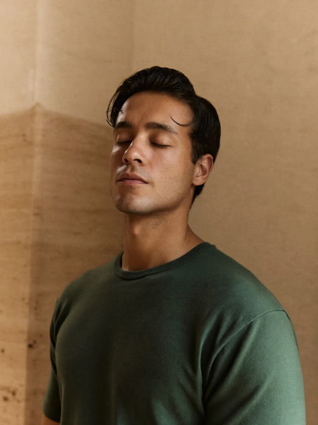 Model in a green T-shirt with eyes closed against a warm plaster wall
