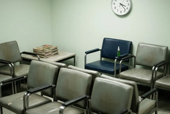 Empty chairs in a clinic waiting room beside a side table stacked with magazines